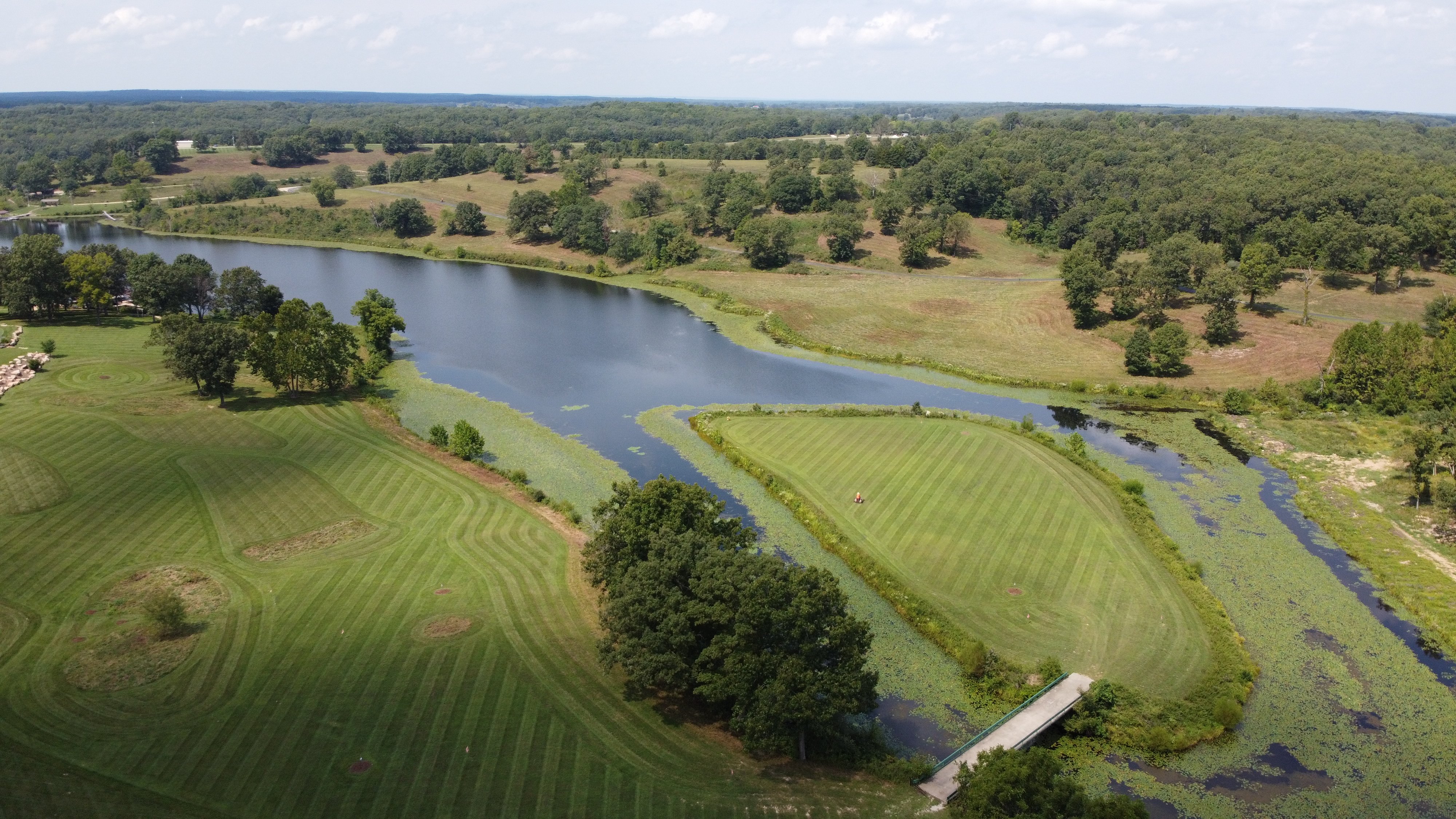 Aerial view of a lakefront estate with wave-striped lawn and stone bridge