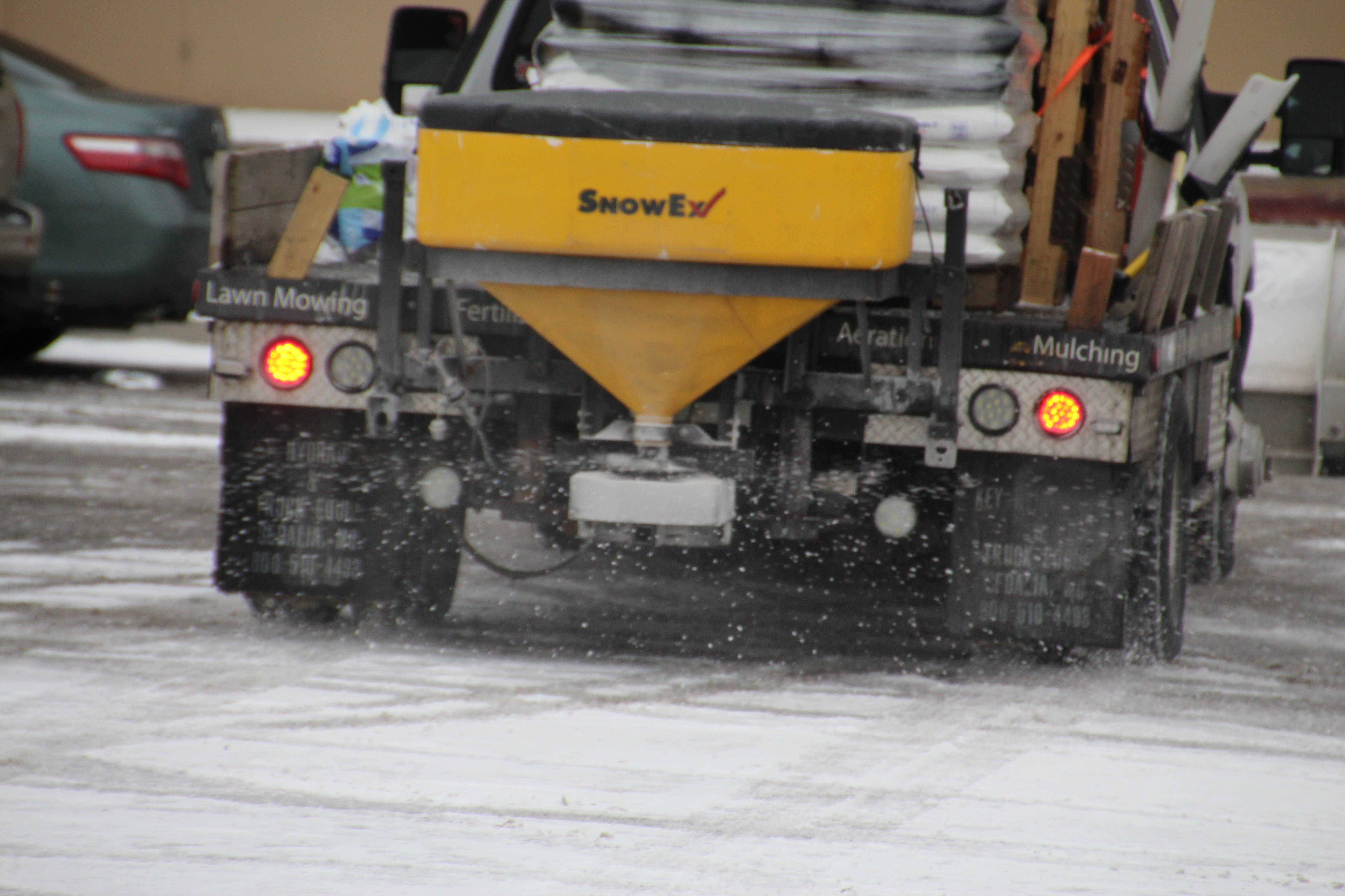 SnowEx salt spreader on a Maedgen's branded flatbed truck in action